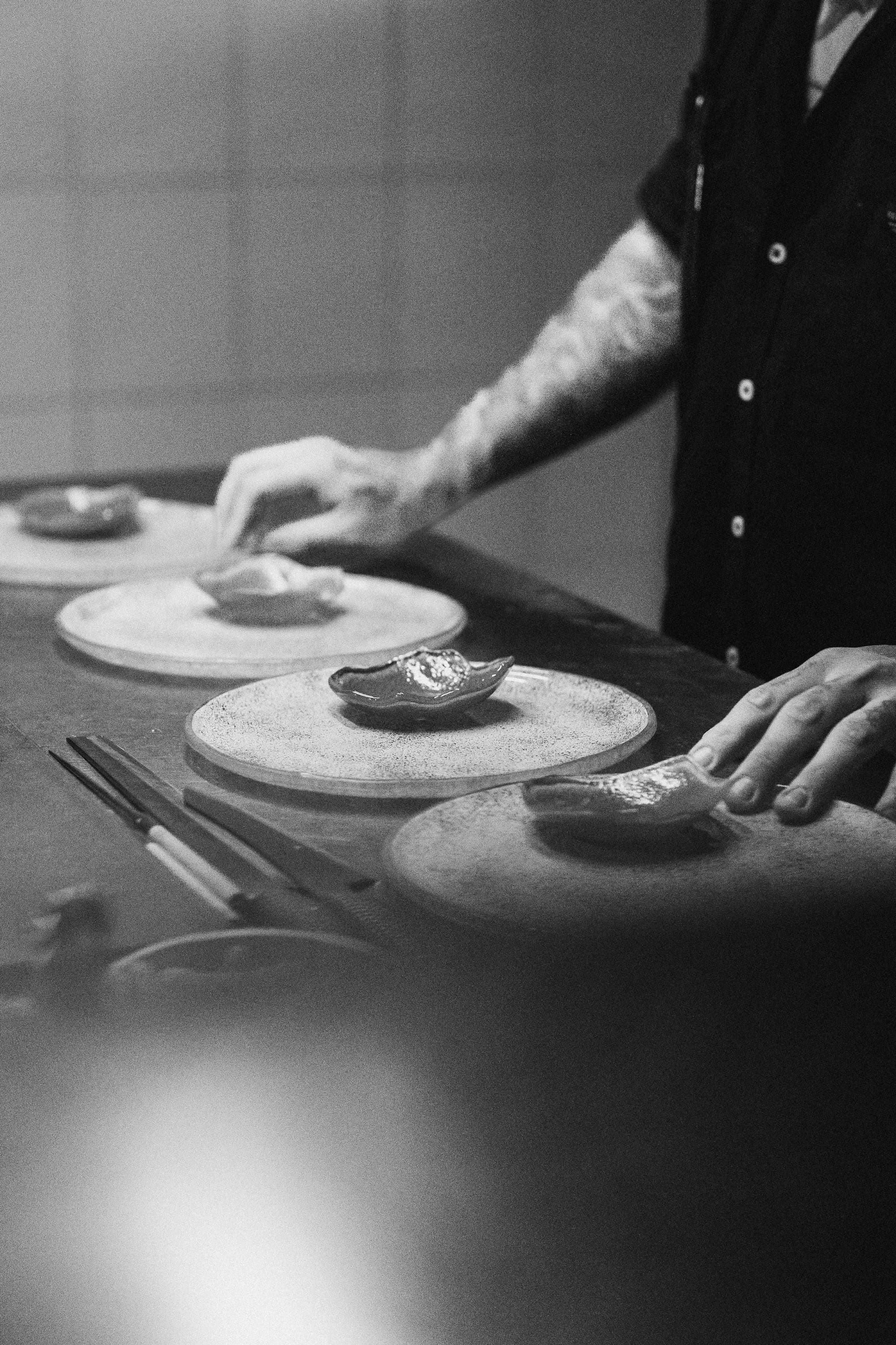 En noir et blanc, des assiettes en céramique dressées une à une sur le passe