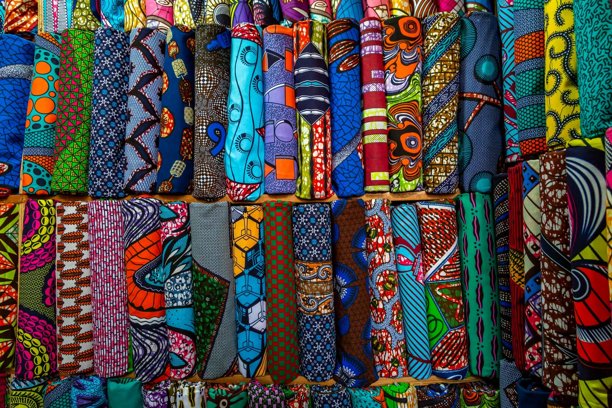 Rouleaux de tissus wax aux motifs colorés empilés sur un étal